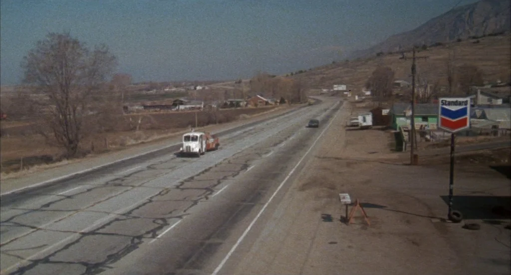 Melvin & Howard (1980) movie still: A wide, high-angle shot captures a lonely stretch of American highway cutting through a barren desert. A single…
