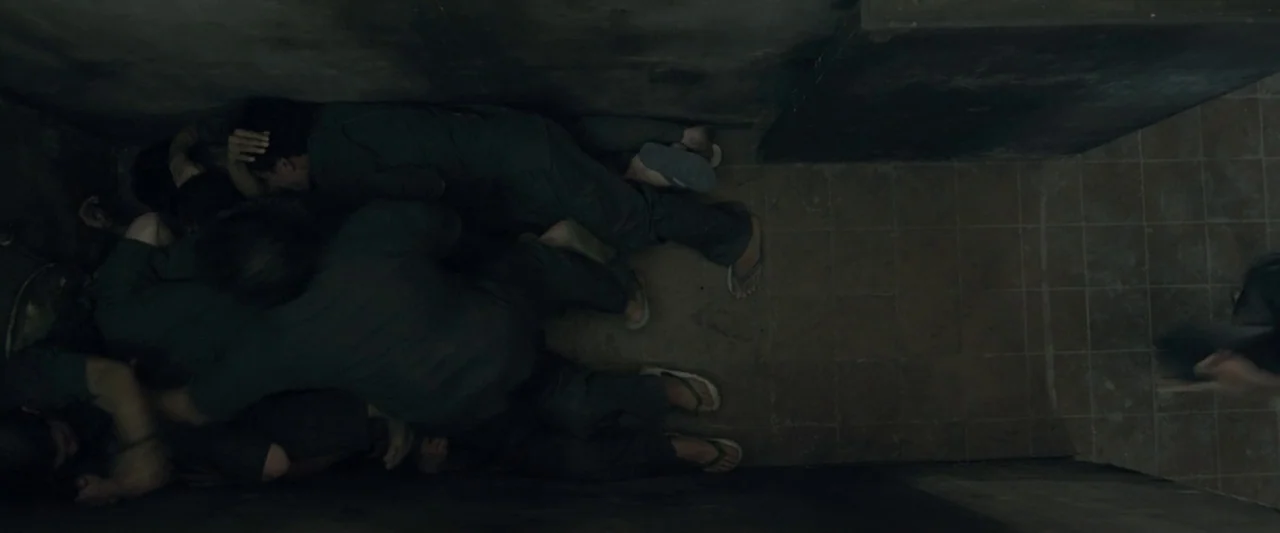 The Raid 2 (2014) movie still: wide — A narrow, windowless enclosure features dark grey walls and dark square floor tiles. Several figures wearing…
