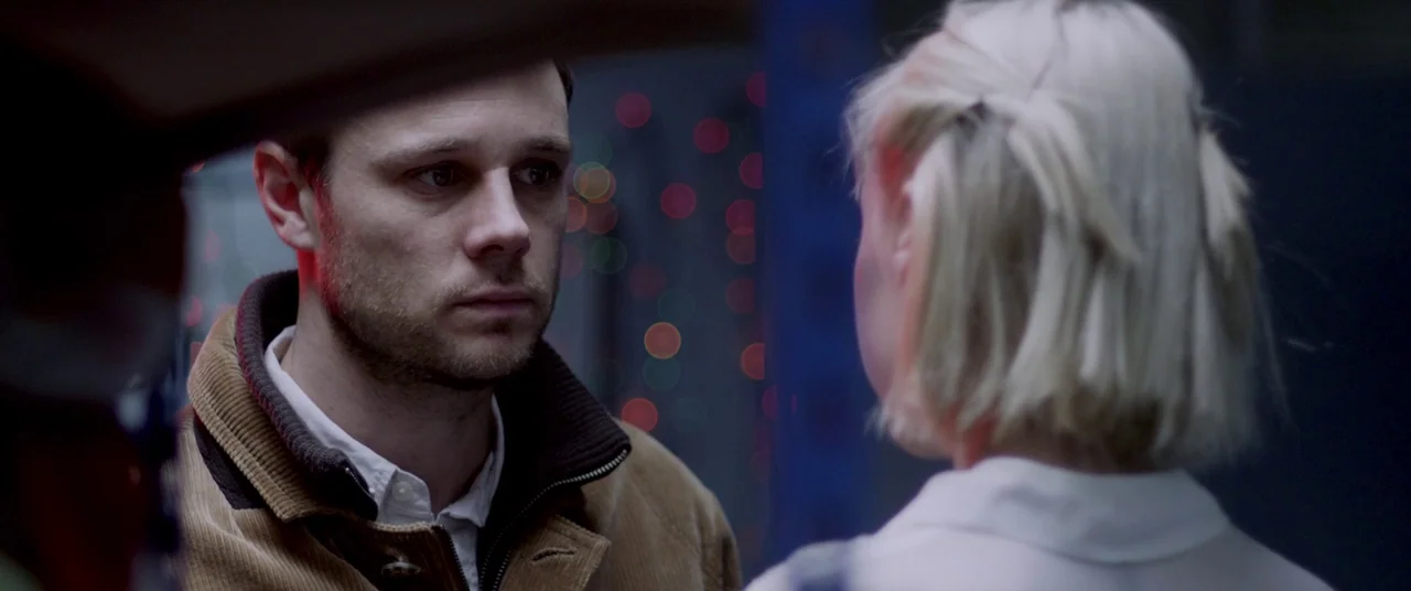 The Canal (2014) movie still: medium — A dark, industrial space filled with blurred points of red and blue light. A man in a brown corduroy jacket…