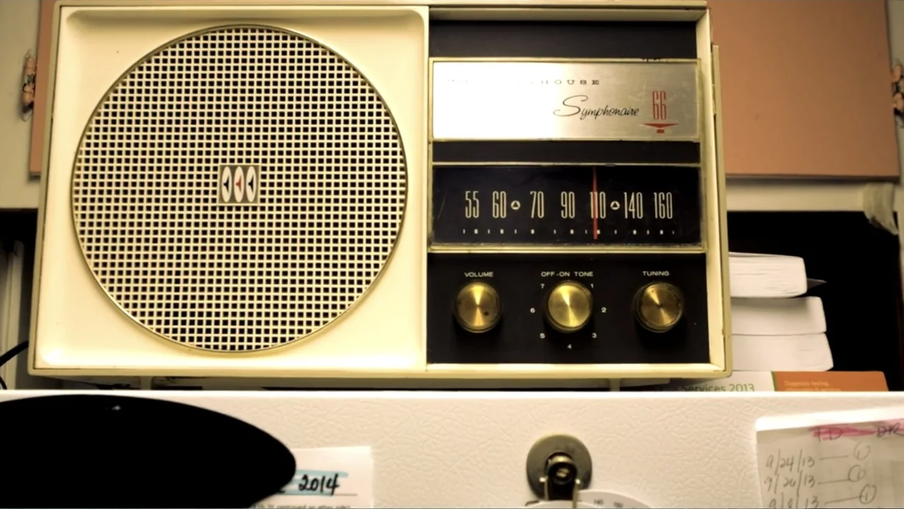Abandoned Dead (2015) movie still: closeup — A white vintage Westinghouse Symphonaire radio sits centered on a desk or shelf. Papers and notes with…