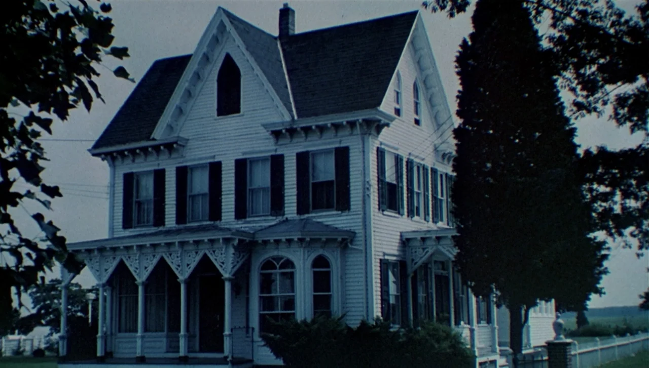 The Dead Zone (1983) movie still: establishing — A white Victorian-style house with dark shutters stands against a backdrop of trees. The house…