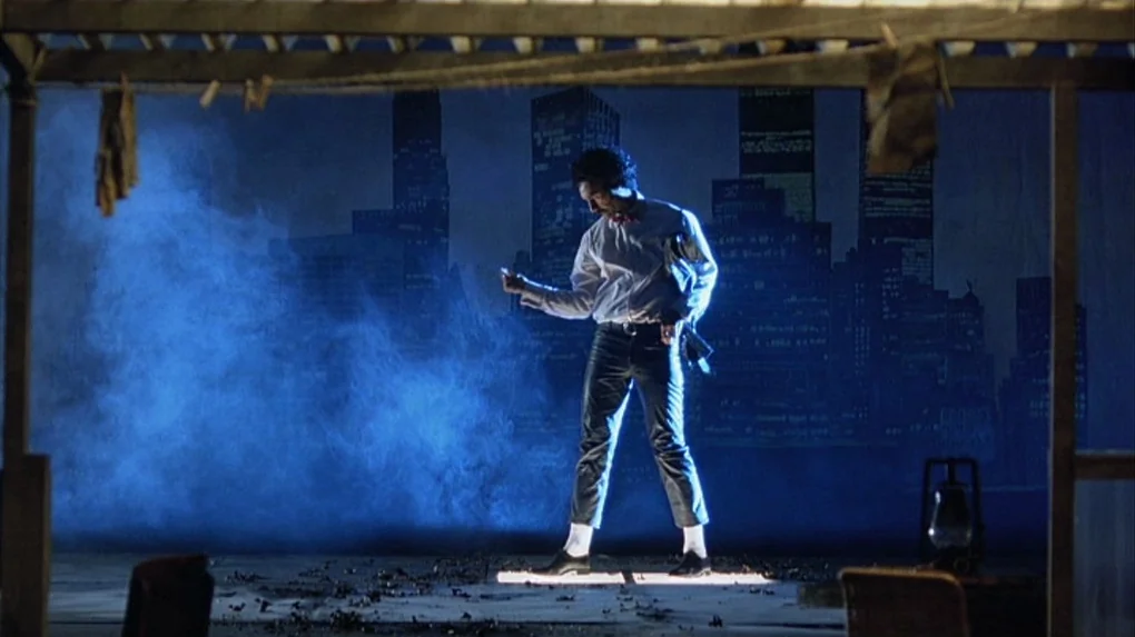 Boy (2010) movie still: fullbody — A dark studio environment features a painted city skyline backdrop and thick stage smoke. The subject stands…