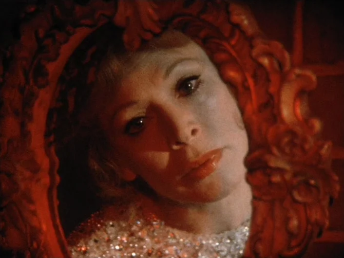 Eika Katappa (1969) movie still: closeup — A woman looks into a small, ornately carved red mirror frame. Her face is centered in the reflection…