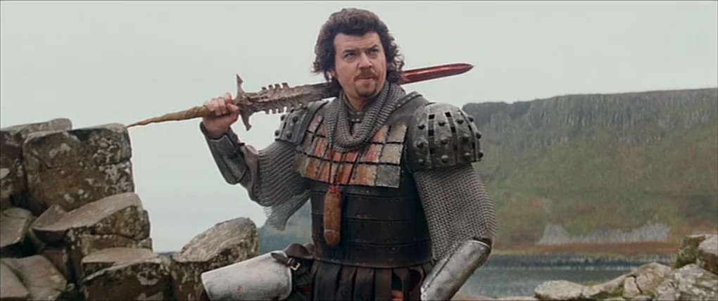 Your Highness (2011) movie still: medium — A man in medieval-style plate and chainmail armor stands on a rugged cliff edge. He rests a large, ornate…