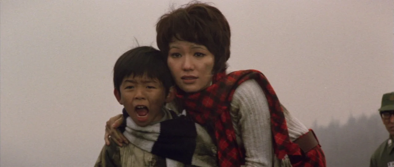 Godzilla Vs Hedorah (1971) movie still: medium — An overcast outdoor location serves as the backdrop for two people in winter clothing. A woman…