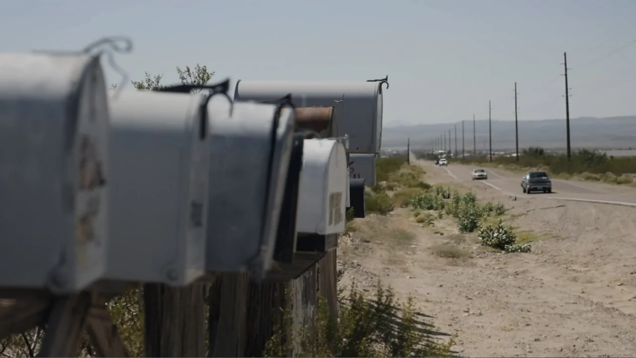 Torn Apart: Separated at the Border (2019) movie still: medium — A line of weathered metal mailboxes sits on wooden posts next to a desert highway.…