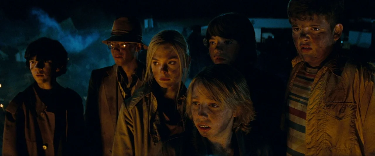 Super 8 (2011) movie still: medium — A group of teenagers stand in a dark, debris-filled landscape lit by fire light. They look toward the distance…