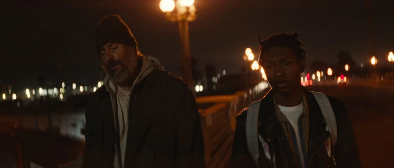 Archenemy (2020) movie still: medium — A bridge at night with multiple streetlights illuminating the dark surroundings. Two men walk closely…