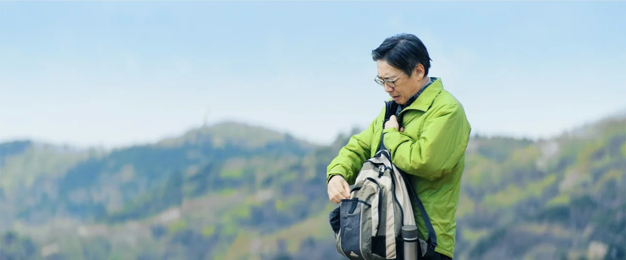 Angel Flight THE MOVIE (2026) movie still: medium — An outdoor mountain landscape provides a backdrop for a hiker during the day. A man in a lime…