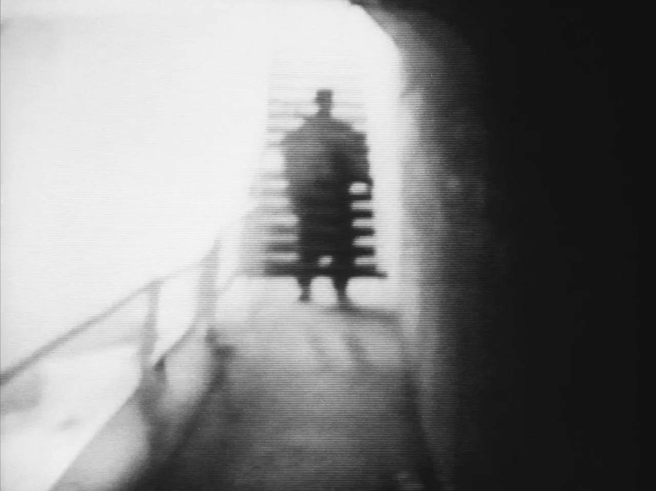 Tetsuo: The Iron Man (1989) movie still: fullbody — A high-contrast staircase features a dark figure positioned against a bright, overexposed light…