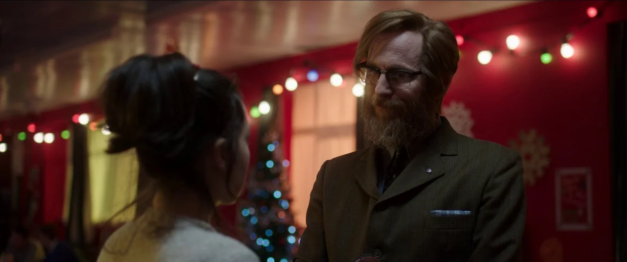 Anna and the Apocalypse (2018) movie still: medium — A festive community hall interior features red walls decorated with string lights and…