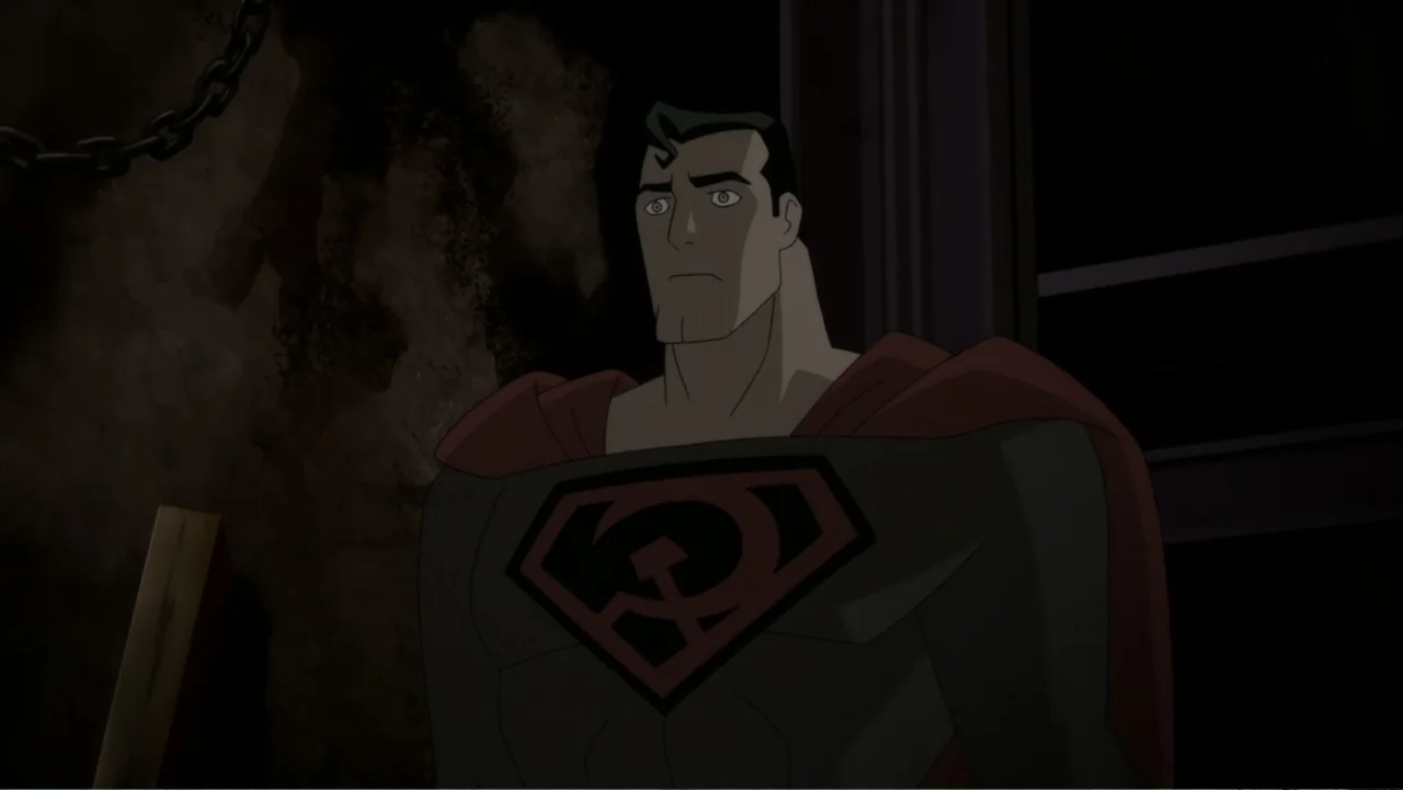 Superman: Red Son (2020) movie still: medium — A dark interior room with rough stone walls and a hanging metal chain. A muscular man in a grey suit…