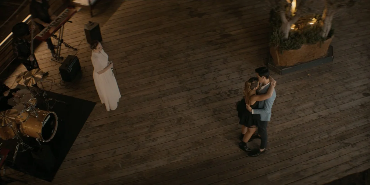 Your Fault (2024) movie still: wide — A wooden outdoor deck serves as a dance floor at night near a band. A couple dances in the center while a…