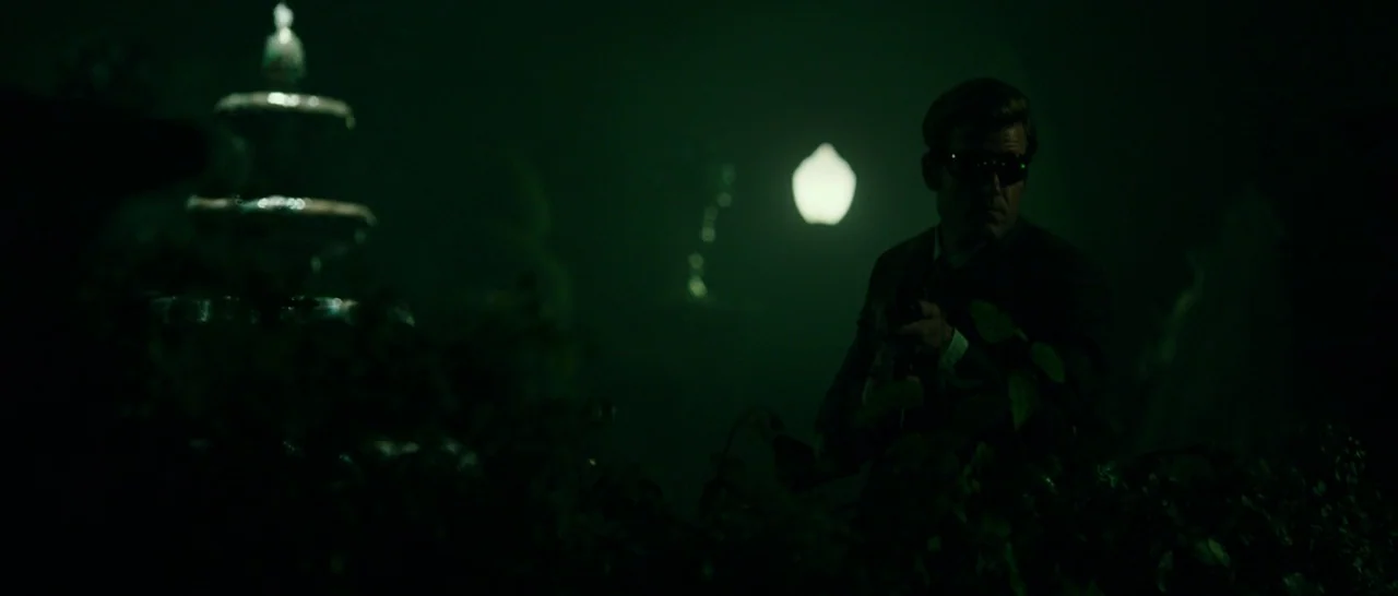 The Purge: Anarchy (2014) movie still: medium — A night scene in a park shows a tiered fountain near thick foliage. A man in a dark suit stands…