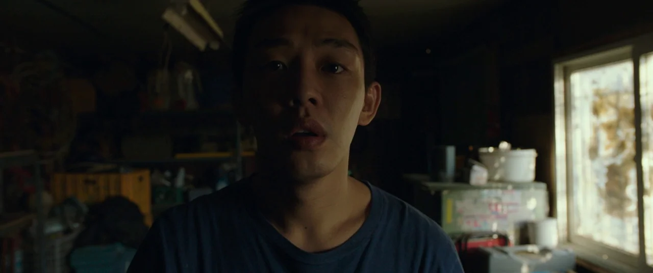 Burning (2018) movie still: closeup — A cluttered storage room contains shelves with various plastic containers and tools in deep shadow. A young…