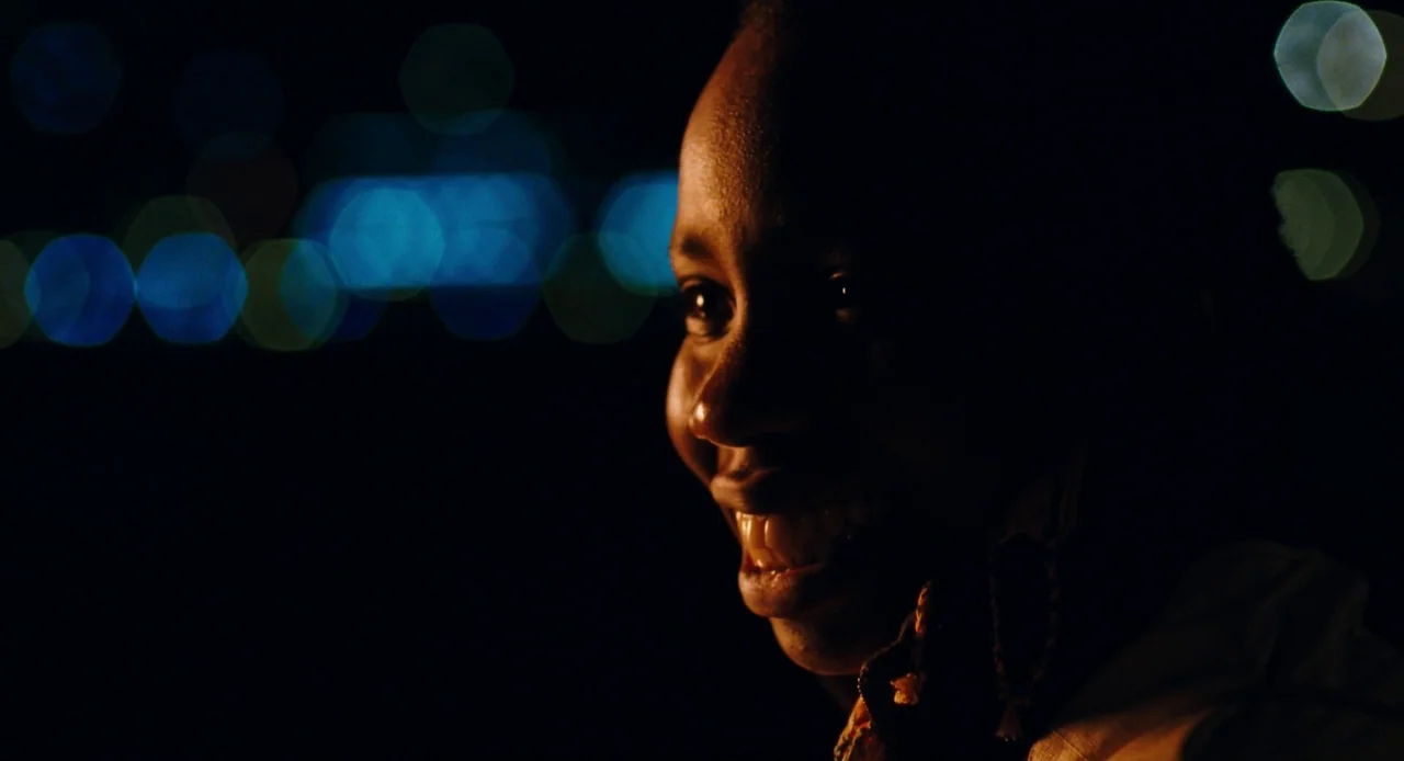Pariah (2011) movie still: closeup — The face of a young woman is illuminated at night against a dark backdrop. Bright circular bokeh in shades of…