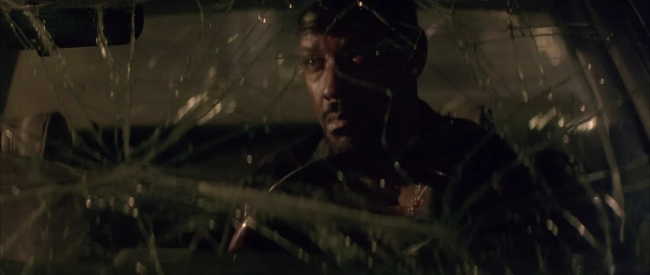 Training Day (2001) movie still: medium — A dark car interior at night with a spiderweb-patterned crack across the windshield. A man sits behind the…