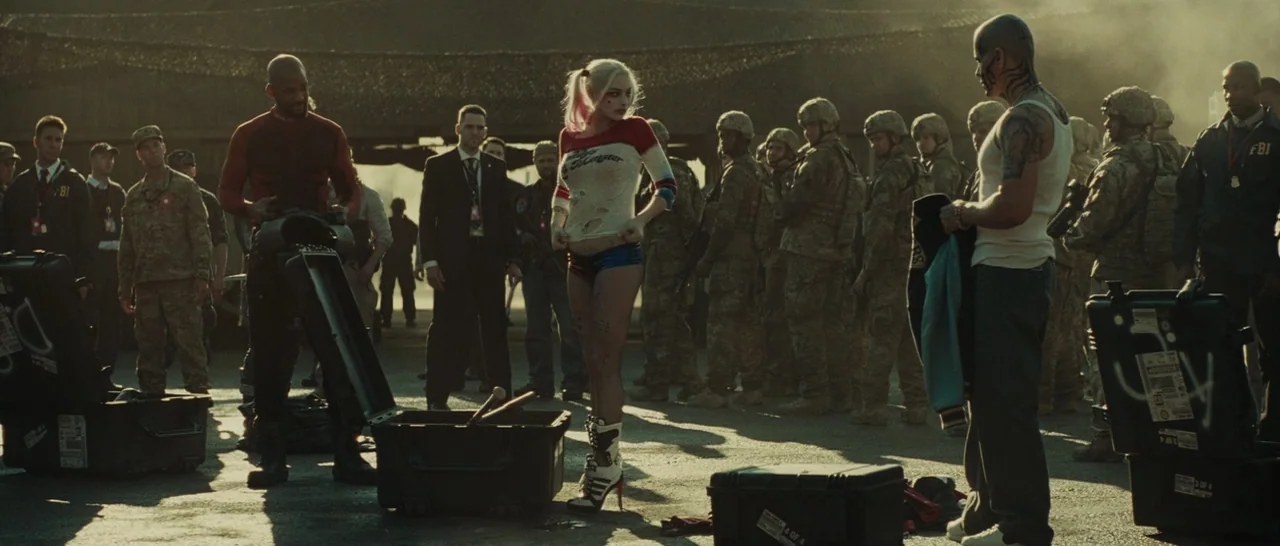 Suicide Squad (2016) movie still: wide — A group of military personnel and individuals stand on a dusty outdoor tarmac area. A woman stands in the…