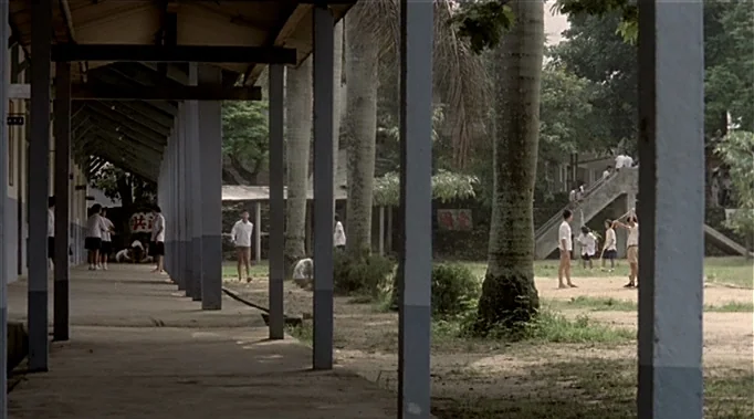 A Time To Love and A Time To Die (1985) movie still: wide — A school courtyard features a concrete walkway with square columns and a sandy play…