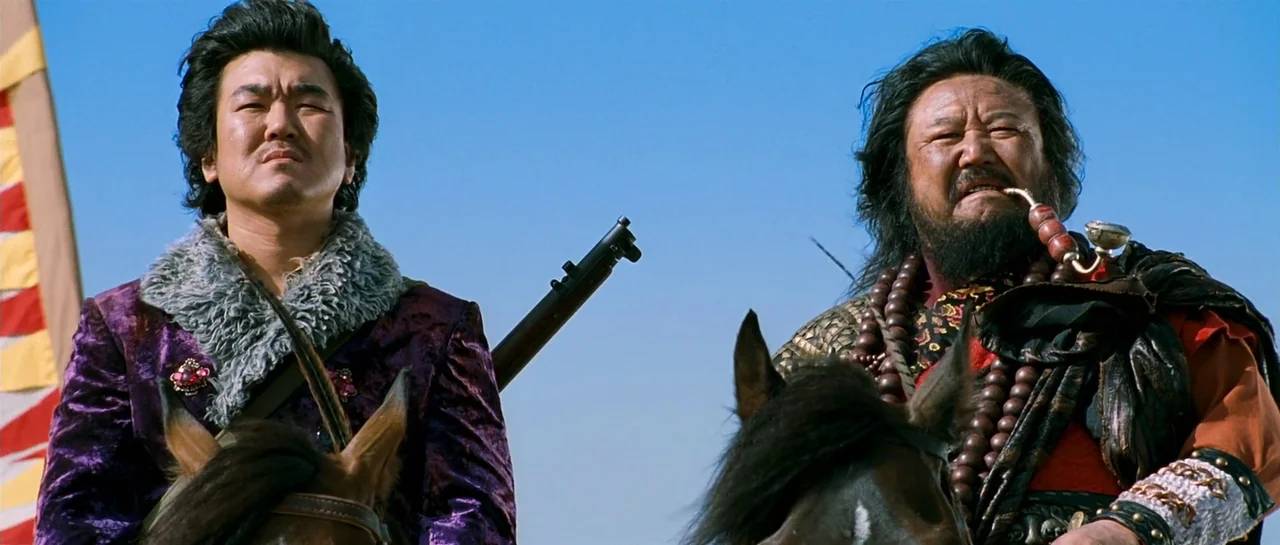The Good The Bad The Weird (2008) movie still: medium — Two men on horseback ride across an arid landscape under a clear sky. The men wear detailed…