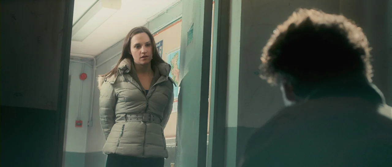 Grabbers (2012) movie still: medium — A school hallway features mint green walls with a map pinned to the wall. A woman wearing a beige winter…
