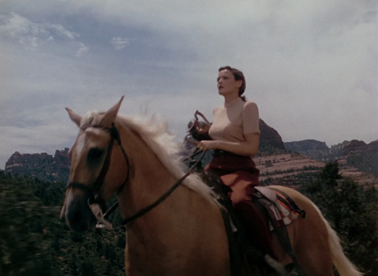 Leave Her To Heaven (1945) movie still: fullbody — A woman on horseback travels through a rocky desert canyon under a cloudy sky. The backdrop…