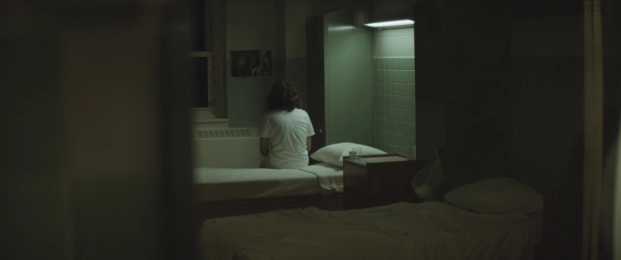 Thoroughbreds (2017) movie still: wide — A dimly lit hospital room features green-tiled walls and metallic storage lockers. A lone individual sits…