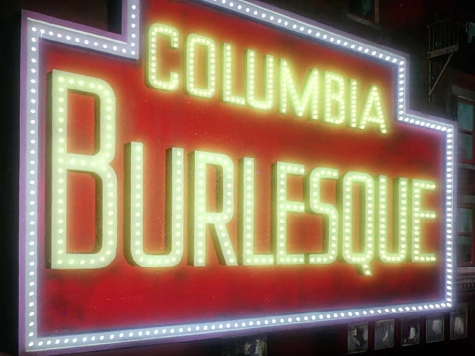 Singin’ in the Rain (1952) movie still: closeup — A large red neon marquee sign spells out Columbia Burlesque in glowing yellow letters. The sign is…