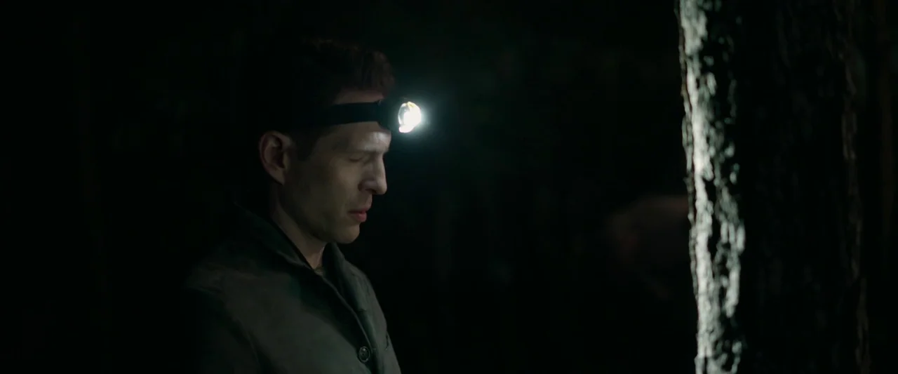 The Hunt (2020) movie still: medium — A man stands in a dark wooded area at night. The man stands with his eyes closed while wearing a bright…
