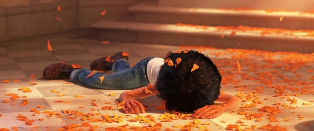 Coco (2017) movie still: medium — A stone-tiled floor is covered with scattered orange marigold petals. A young boy lies facedown on the tiles, his…