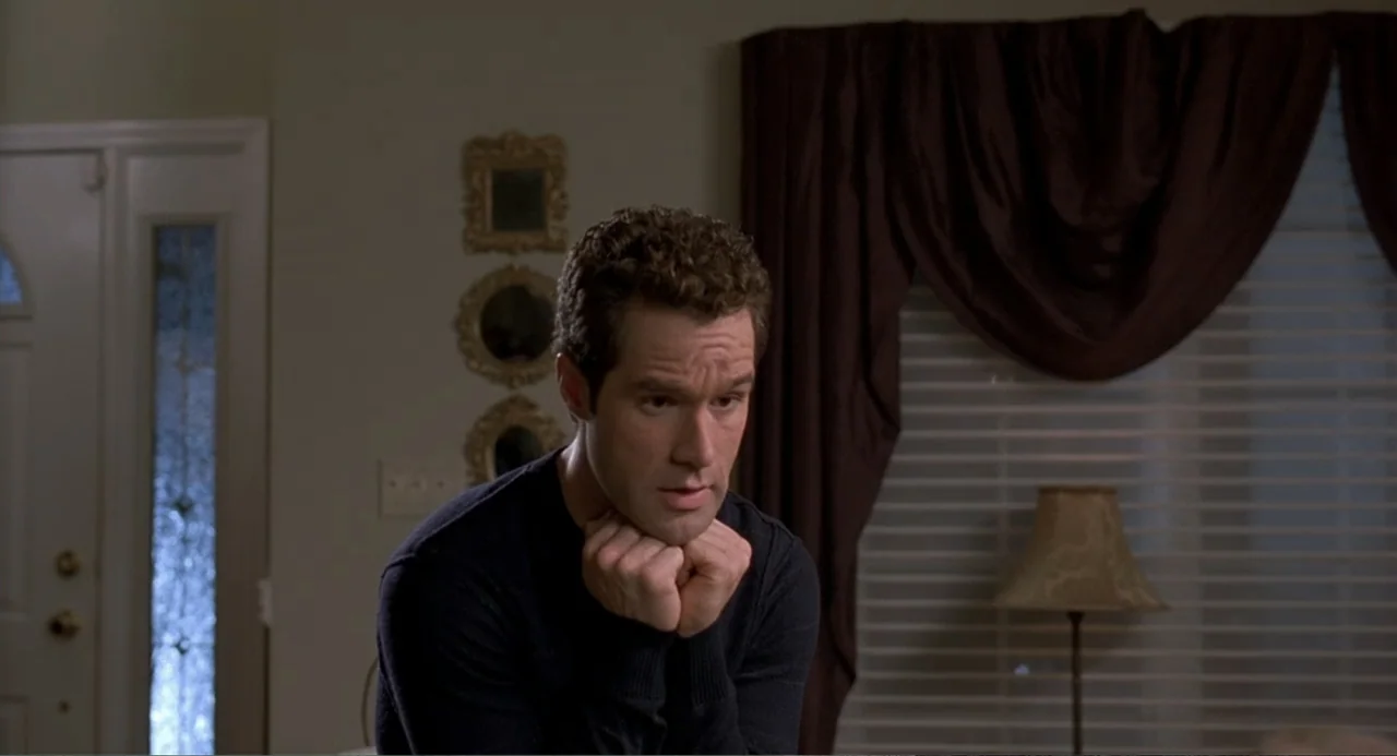 Wedding Daze (2006) movie still: medium — A residential interior features a doorway and dark curtains covering a window. A man in a dark sweater…