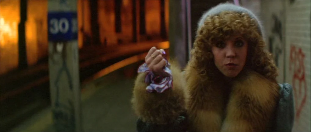 Blow Out (1981) movie still: medium — A night view of a concrete subway platform with distant golden platform lighting. A young woman with curly…