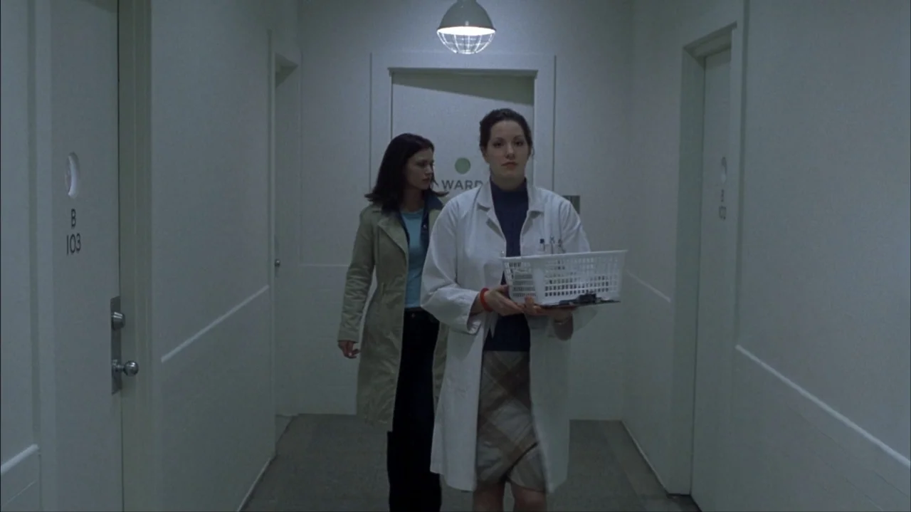 Final Destination 2 (2003) movie still: medium — A sterile hospital corridor with pale walls and closed doors on both sides. A woman in a white lab…