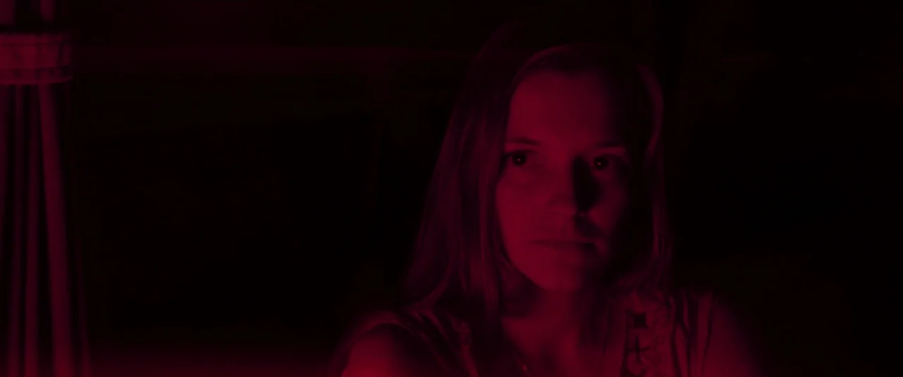 Mandy (2018) movie still: closeup — A woman is situated in a dark space featuring a heavy draped curtain. She is looking slightly off-camera while…
