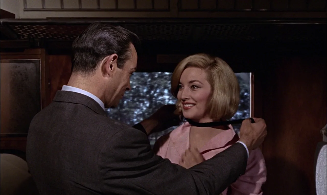 From Russia With Love (1963) movie still: medium — A wood-paneled train cabin features a window looking out onto blurred exterior landscape scenery.…