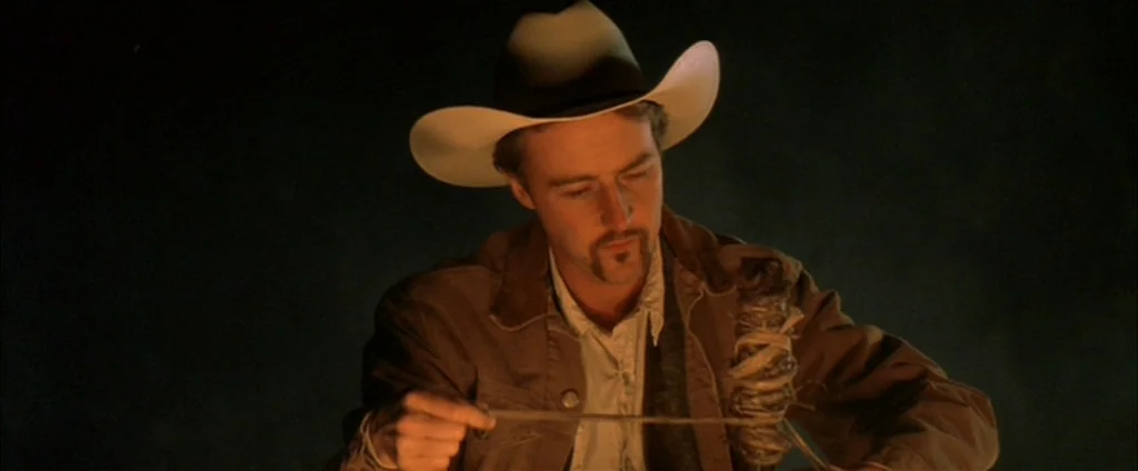 Down In The Valley (2005) movie still: medium — An outdoor night setting is dark with only the immediate foreground illuminated by fire. A man in a…