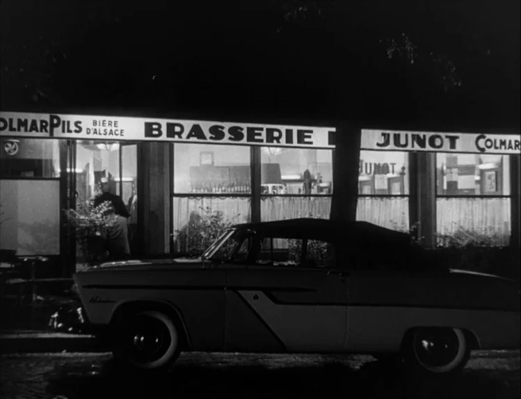 Bob le Flambeur (1956) movie still: wide — A nighttime view of a French brasserie storefront with large glass windows and signage. A classic…