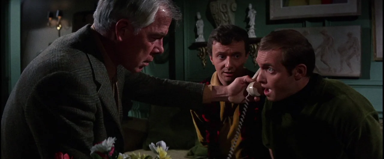 Point Blank (1967) movie still: medium — A dimly lit room with green walls featuring decorative wall art and small figurines. An older man leans…