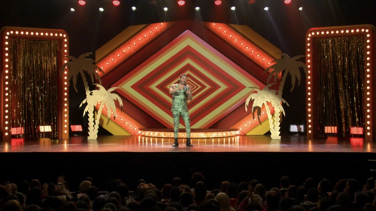 Felipe Avello: Doglover (2024) movie still: fullbody — A brightly lit stage features large stylized palm tree cutouts and a geometric patterned…