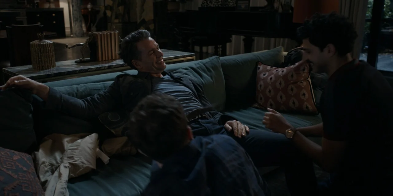 The People We Hate at the Wedding (2022) movie still: medium — A dimly lit modern living room with a large teal sofa and dark wood furniture. Three…