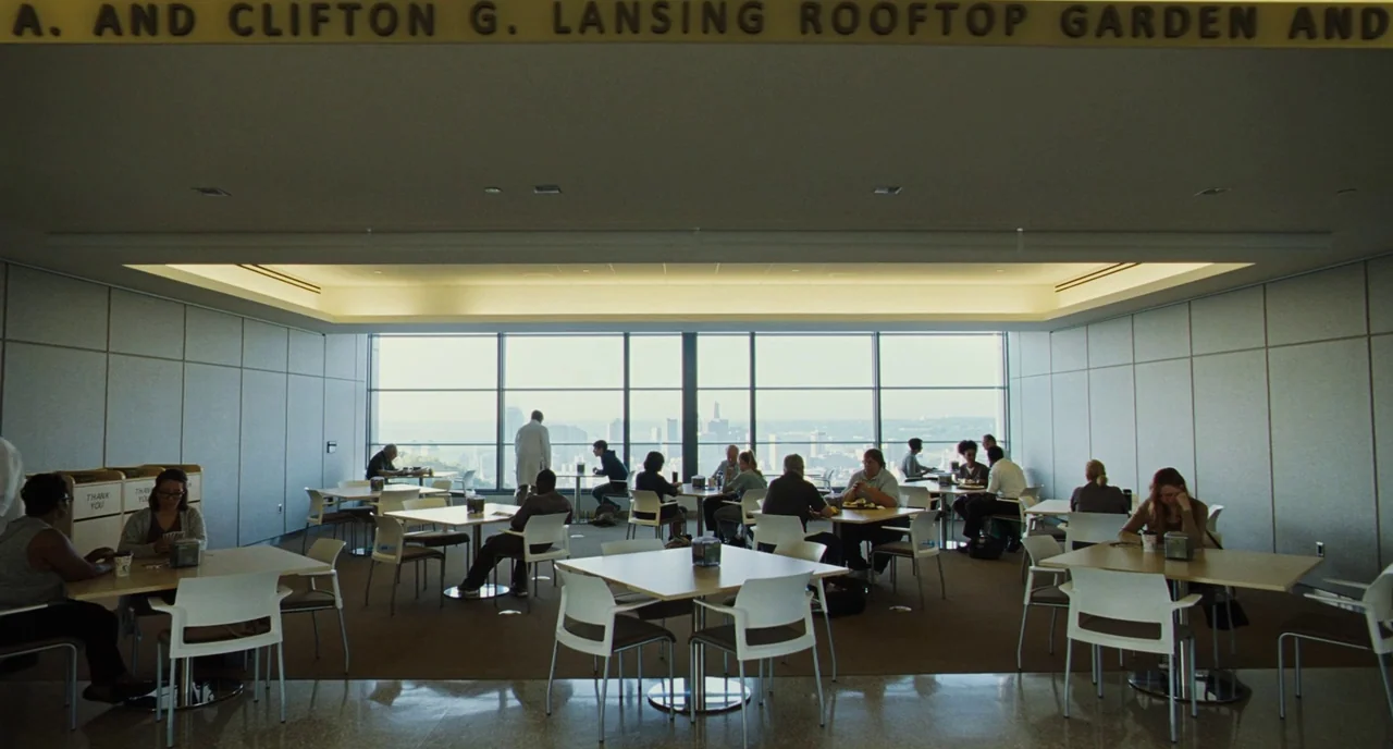 The Killing of a Sacred Deer (2017) movie still: wide — A bright, modern cafeteria with square tables and white chairs under a low ceiling. People…