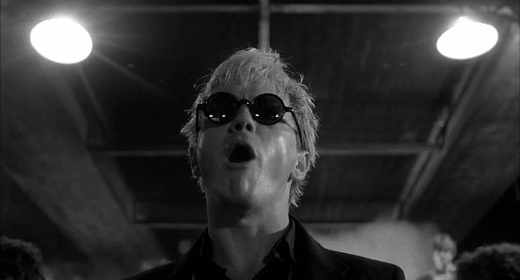 Rumble Fish (1983) movie still: closeup — An outdoor concrete underpass at night illuminated by two intense overhead artificial lamps. A man with…