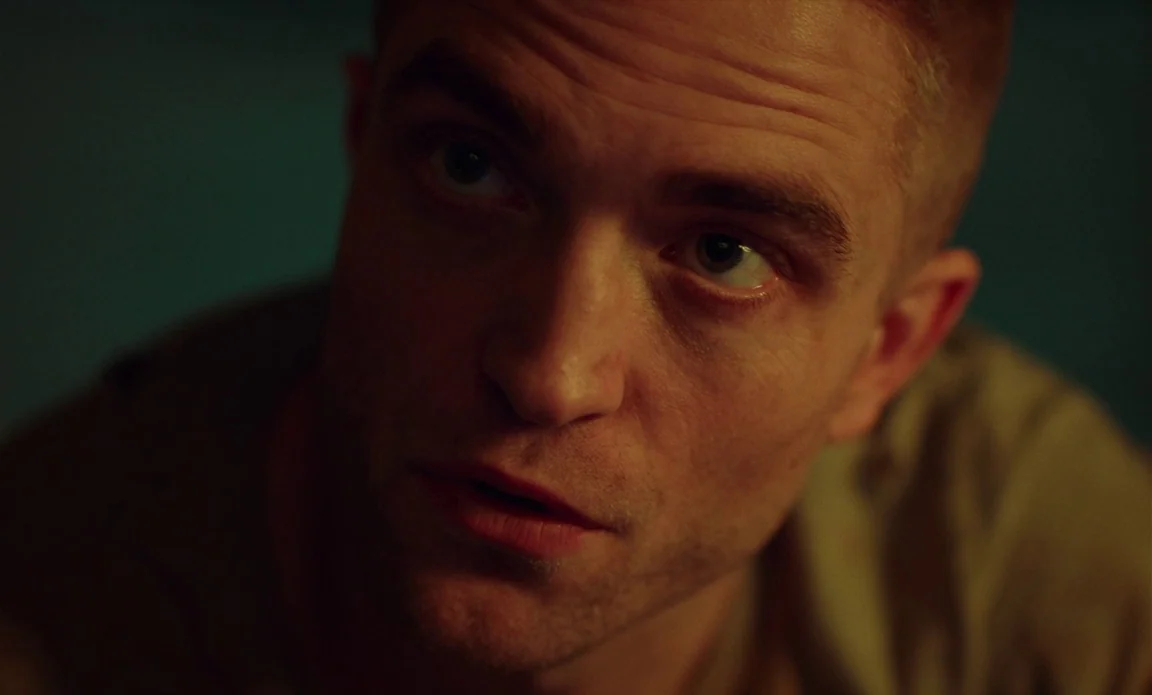 High Life (2018) movie still: closeup — A dark indoor space is lit by a soft, warm light source. A man with short hair gazes upward with his mouth…