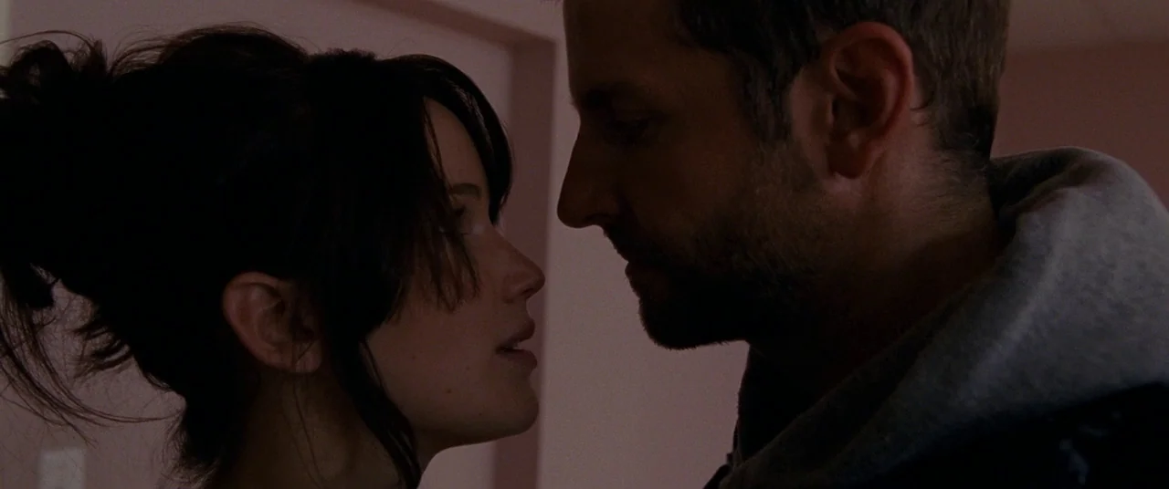 Silver Linings Playbook (2012) movie still: closeup — A man and a woman stand close together in a softly lit interior space. They are positioned in…