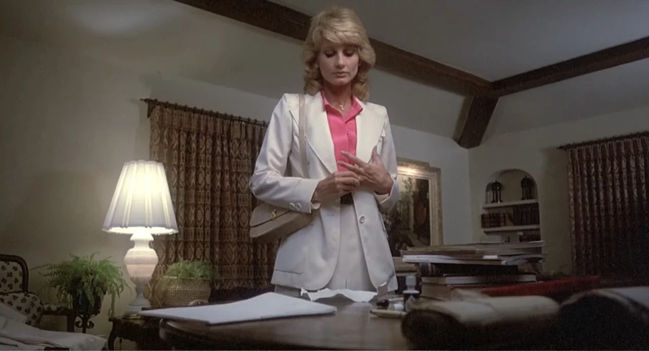 Death Wish II (1982) movie still: medium — A traditional office features wooden beams, beige walls, and a desk covered in papers. A woman stands in…