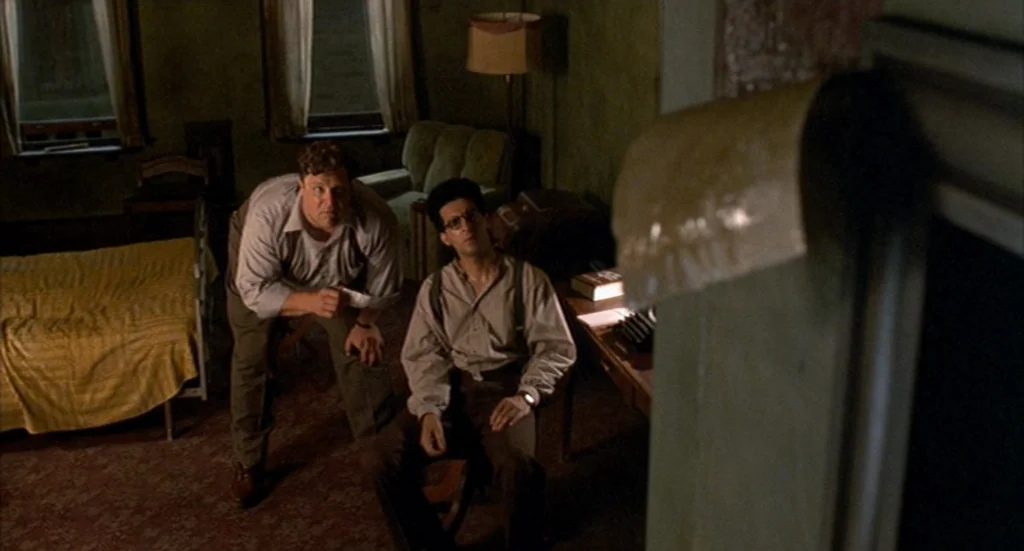 Barton Fink (1991) movie still: medium — A dimly lit, claustrophobic 1940s hotel room features patterned carpet and sparse vintage furniture. Two…