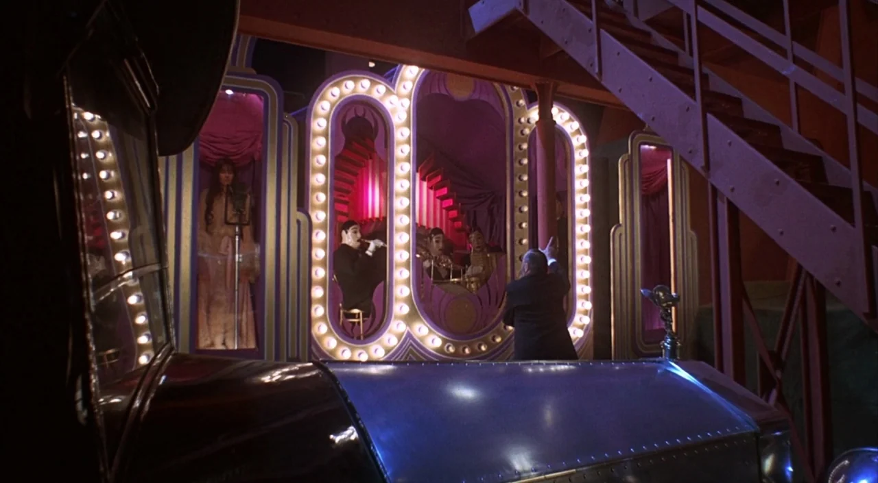 Dr. Phibes Rises Again (1972) movie still: wide — A theatrical set features illuminated art deco panels with performers framed in glowing niches. A…
