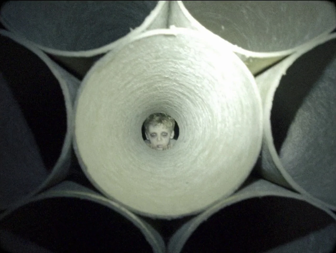 The Devil’s Doorway (2018) movie still: closeup — A cluster of stacked, open-ended cardboard paper towel rolls creates a tunnel effect. A small…