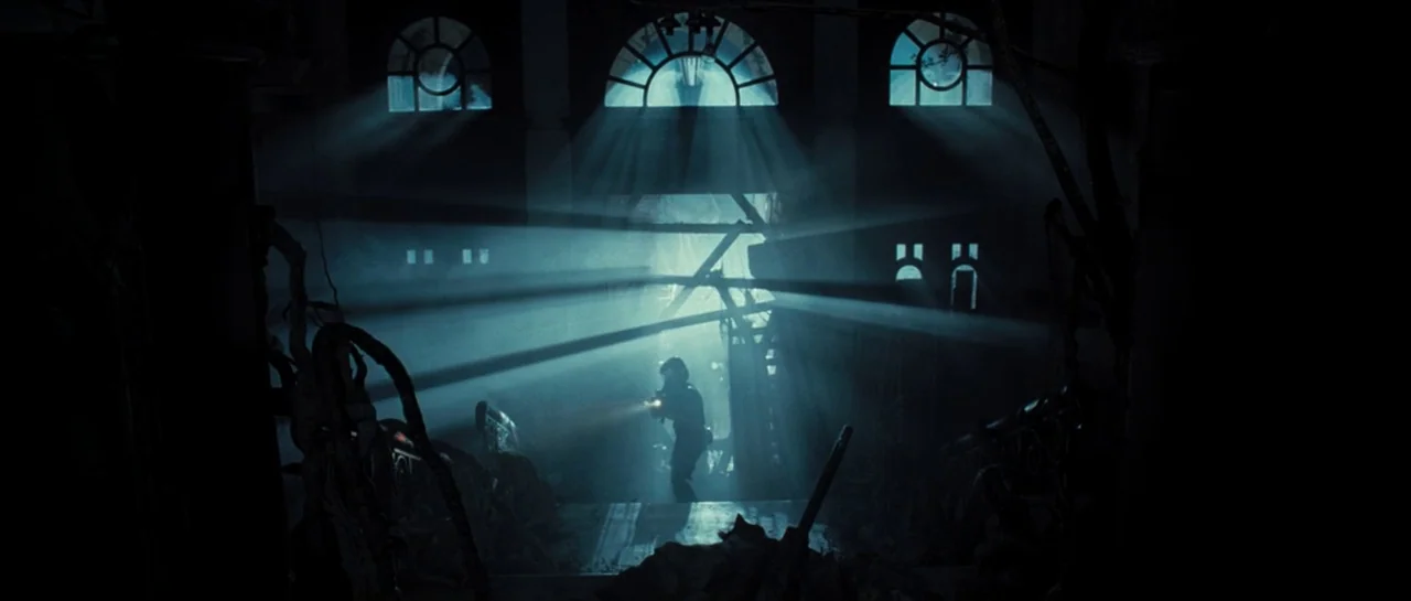 Doomsday (2008) movie still: wide — A dark, dilapidated foyer with arched windows and debris scattered across the floor. A lone figure equipped with…