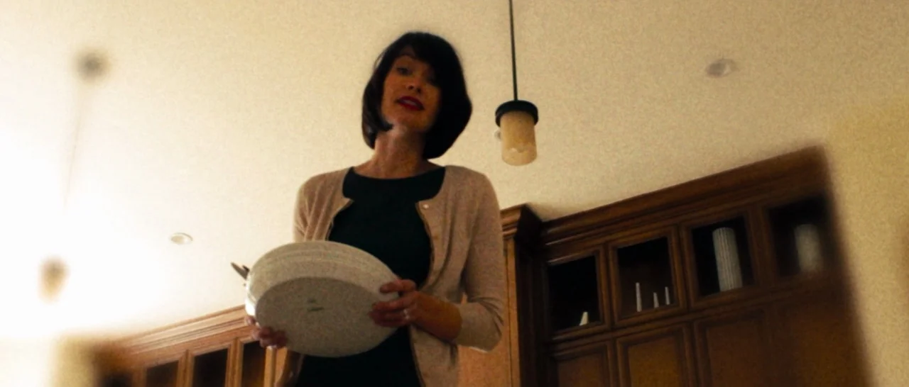 The Purge (2013) movie still: medium — A woman stands in a room with wooden cabinetry and a hanging pendant lamp. She holds a white ceramic bowl in…